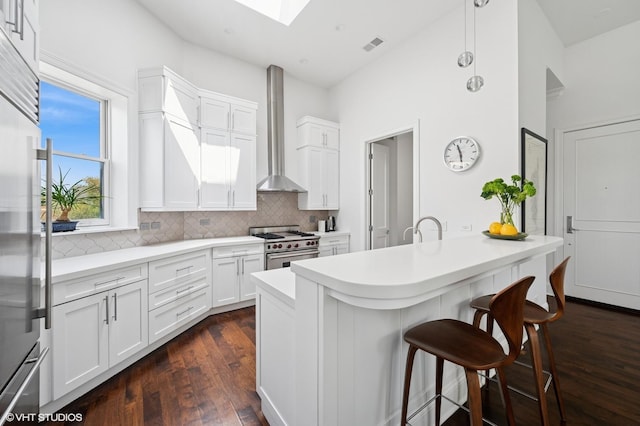 kitchen featuring premium appliances, wall chimney exhaust hood, a skylight, a breakfast bar area, and backsplash