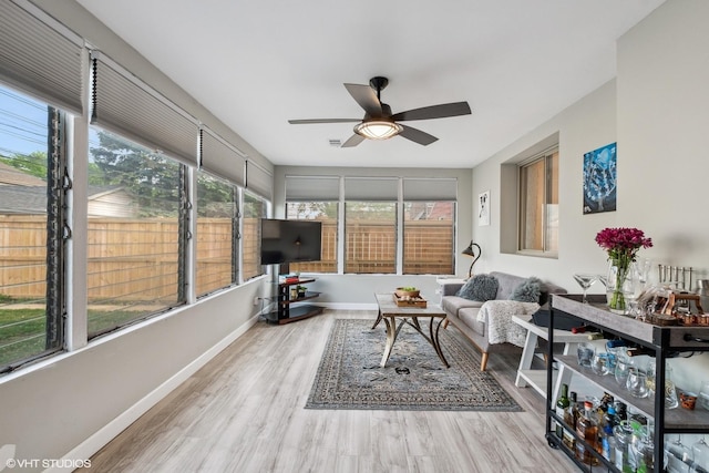 sunroom featuring a ceiling fan, wood finished floors, baseboards, and an outdoor hangout area