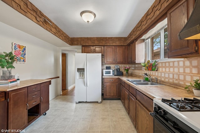 kitchen featuring white appliances, a sink, under cabinet range hood, light countertops, and decorative backsplash