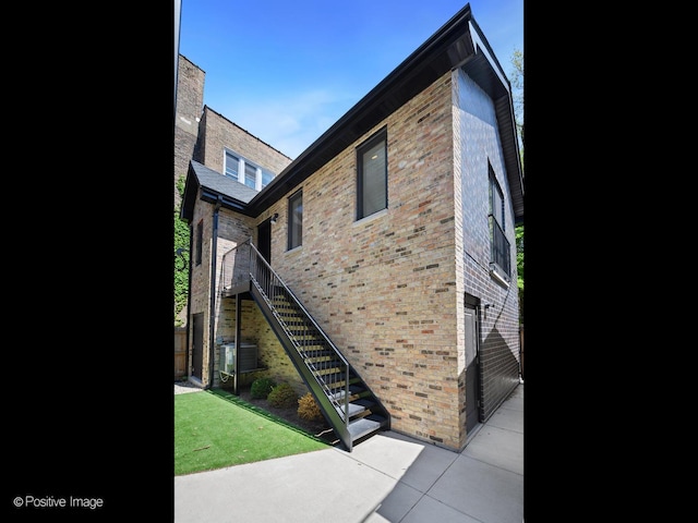view of side of property featuring brick siding, stairway, and a patio