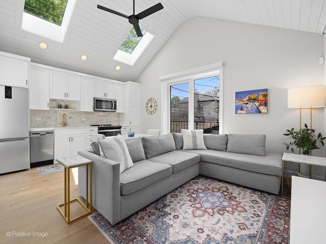 living area with light wood finished floors, a skylight, recessed lighting, high vaulted ceiling, and ceiling fan