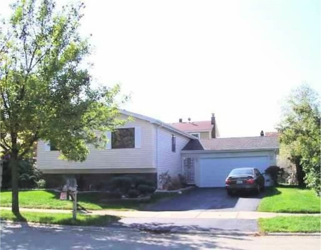 split level home with asphalt driveway, a garage, and a front lawn
