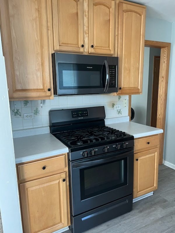 kitchen featuring black gas range, light brown cabinets, light countertops, light wood-style flooring, and tasteful backsplash
