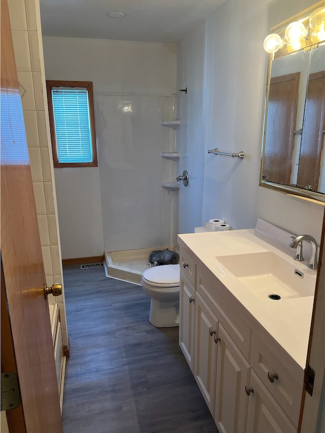 bathroom featuring toilet, a shower, wood finished floors, and vanity