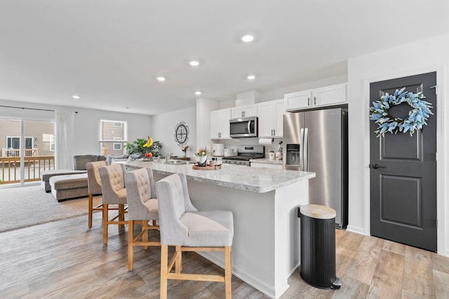 1447 Yosemite Way, Pingree Grove, IL 60140 - kitchen with appliances with stainless steel finishes, a breakfast bar area, white cabinetry, an island with sink, and light wood finished floors