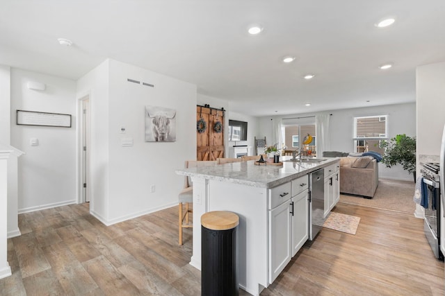 1447 Yosemite Way, Pingree Grove, IL 60140 - kitchen with appliances with stainless steel finishes, a barn door, light wood finished floors, a kitchen breakfast bar, and recessed lighting