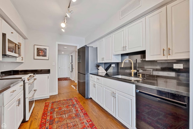 kitchen featuring a sink, double oven range, dishwasher, freestanding refrigerator, and white cabinets
