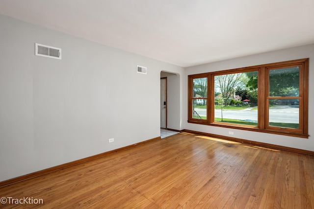 empty room with arched walkways, baseboards, and light wood-type flooring