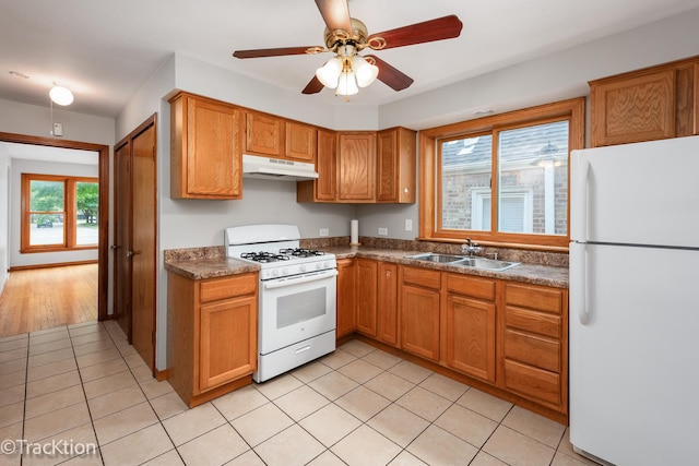 kitchen with white appliances, a sink, under cabinet range hood, light tile patterned floors, and brown cabinets