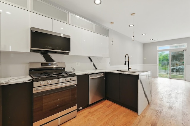 kitchen with appliances with stainless steel finishes, modern cabinets, a peninsula, white cabinetry, and light wood-type flooring