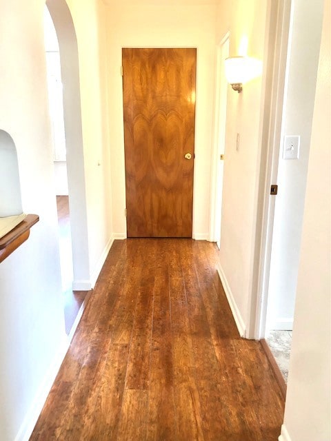 corridor featuring arched walkways, wood-type flooring, and baseboards