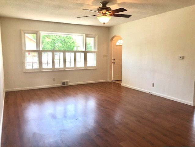 empty room with arched walkways, ceiling fan, dark wood-type flooring, and baseboards