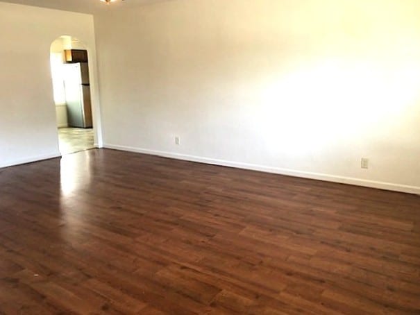 unfurnished room with arched walkways, dark wood-style flooring, and baseboards