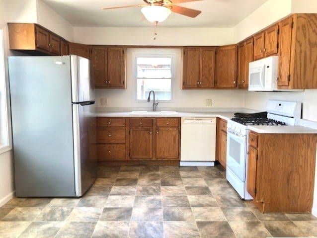 kitchen with white appliances, a sink, a ceiling fan, brown cabinetry, and light countertops