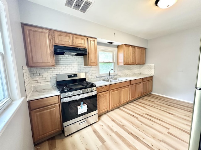 301 Illinois Ave, Elgin, IL 60120 - kitchen with stainless steel gas stove, under cabinet range hood, a sink, light wood finished floors, and light countertops