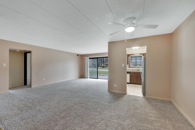 spare room with light colored carpet, a ceiling fan, baseboards, and a sink