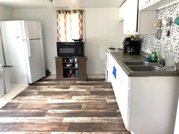 kitchen featuring white appliances, white cabinetry, a sink, light wood-style floors, and dark countertops