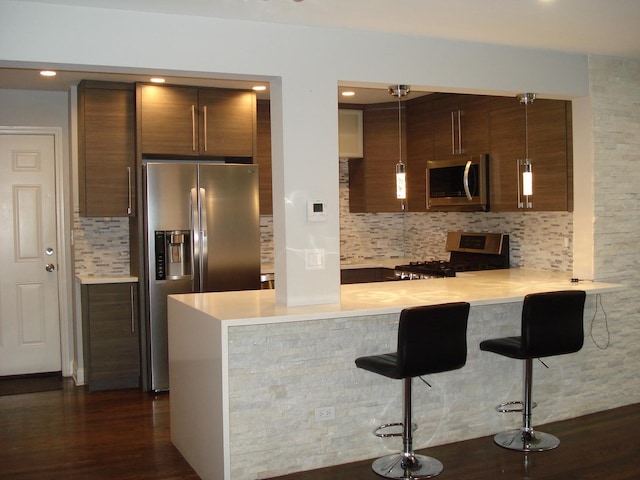 kitchen featuring appliances with stainless steel finishes, tasteful backsplash, a kitchen bar, light countertops, and a peninsula