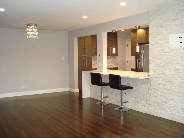 kitchen with stainless steel refrigerator with ice dispenser, a breakfast bar area, a peninsula, dark wood-style floors, and light countertops