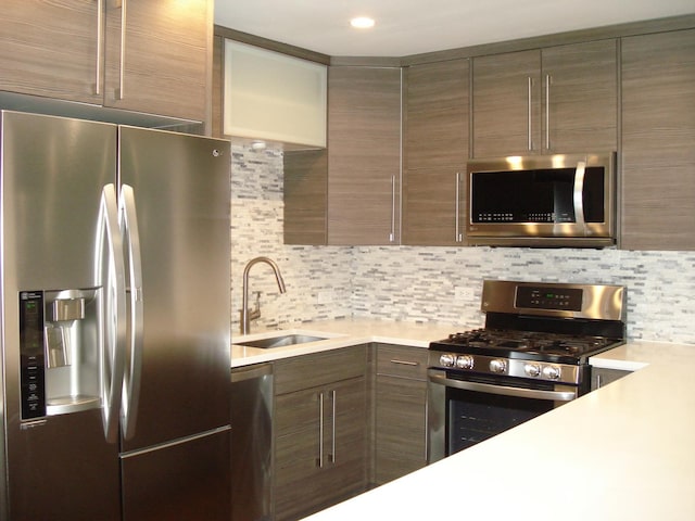 kitchen featuring appliances with stainless steel finishes, a sink, modern cabinets, light countertops, and tasteful backsplash