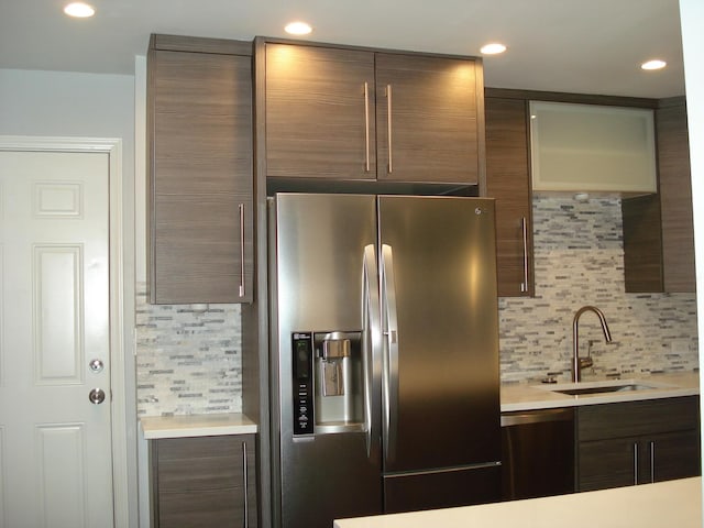 kitchen featuring stainless steel refrigerator with ice dispenser, a sink, tasteful backsplash, light countertops, and dishwashing machine