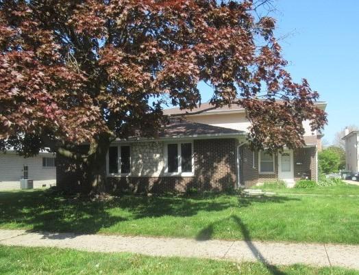 view of property hidden behind natural elements featuring a front lawn and brick siding