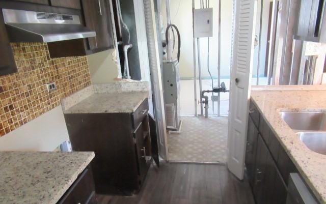 kitchen with under cabinet range hood, dark brown cabinetry, tasteful backsplash, electric panel, and light stone countertops