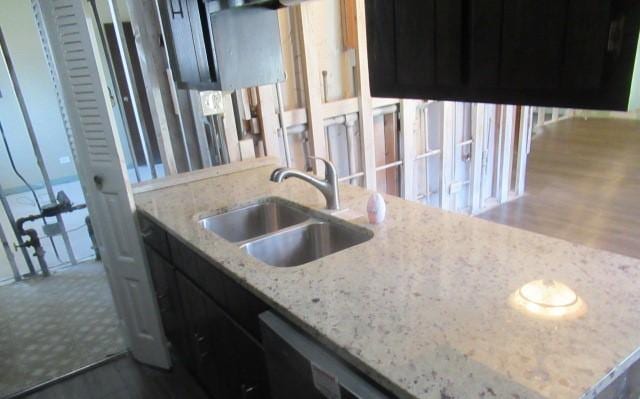 kitchen featuring a sink, wood finished floors, dark cabinetry, and light stone countertops