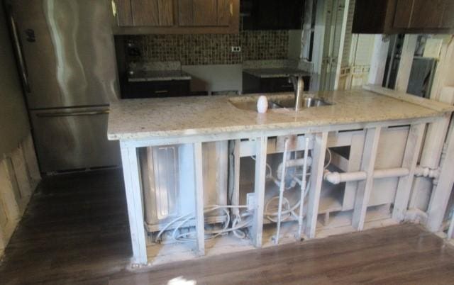 kitchen featuring freestanding refrigerator, tasteful backsplash, wood finished floors, light stone counters, and a sink