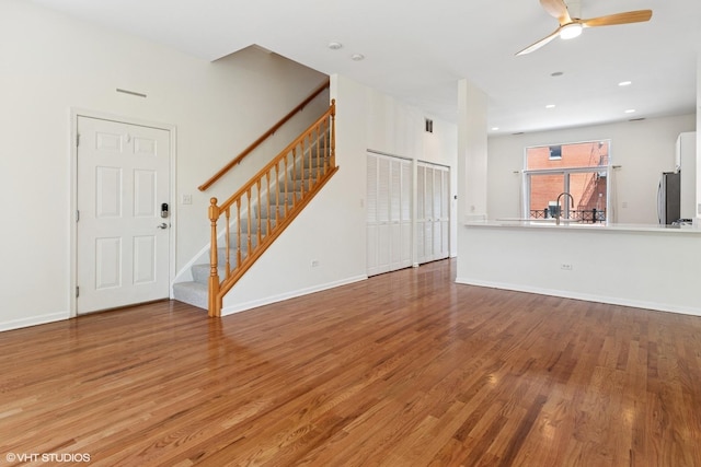 unfurnished living room featuring wood finished floors, ceiling fan, stairway, baseboards, and a sink