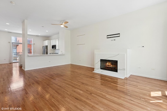 unfurnished living room with light wood finished floors, a fireplace, ceiling fan, baseboards, and recessed lighting