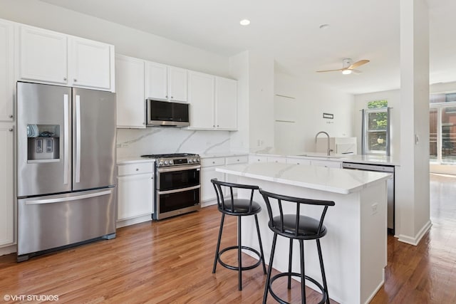 kitchen with stainless steel appliances, a sink, light wood-type flooring, a kitchen breakfast bar, and white cabinetry