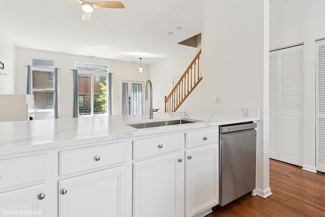 kitchen with stainless steel dishwasher, a sink, dark wood-type flooring, light stone counters, and white cabinets