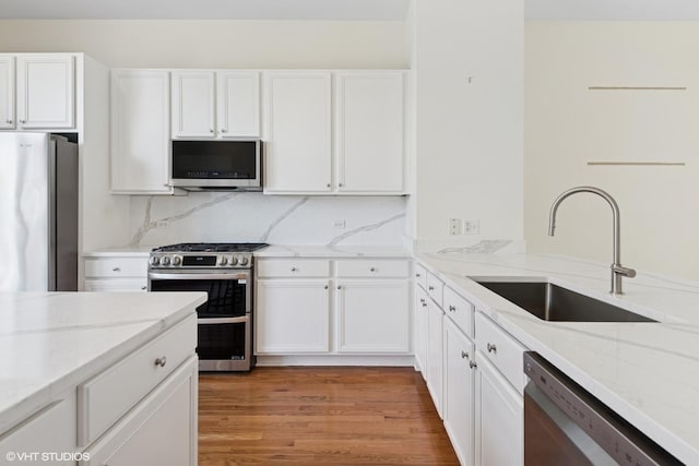 kitchen with stainless steel appliances, a sink, white cabinetry, light stone counters, and light wood-style floors