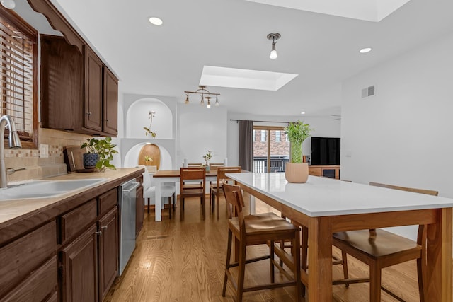 7260 W Fitch Ave, Chicago, IL 60631 - kitchen featuring a skylight, dishwasher, a sink, light wood-style floors, and decorative backsplash