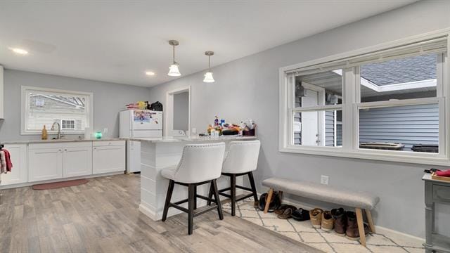 801 Adams St, Oregon, IL 61061 - kitchen with white cabinetry, freestanding refrigerator, a breakfast bar, light wood-style flooring, and pendant lighting