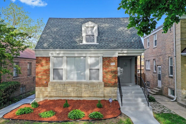view of front of home with a shingled roof, fence, brick siding, and stone siding