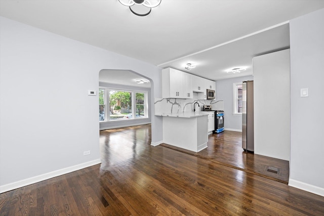 unfurnished living room featuring arched walkways, dark wood finished floors, and baseboards