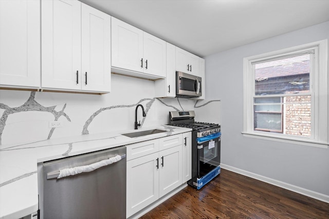 kitchen with appliances with stainless steel finishes, a sink, light stone counters, and white cabinets