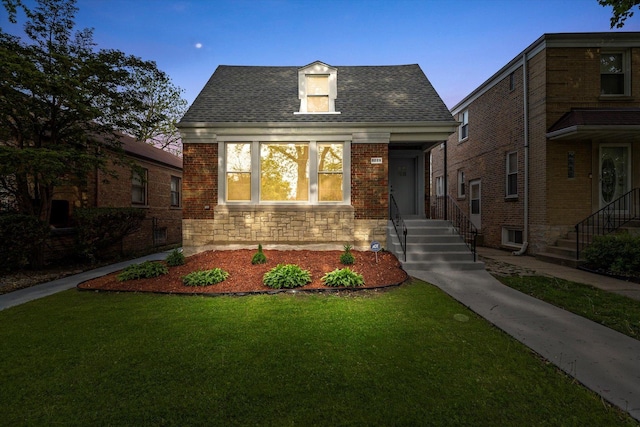 view of front facade with a front lawn, roof with shingles, stone siding, and brick siding