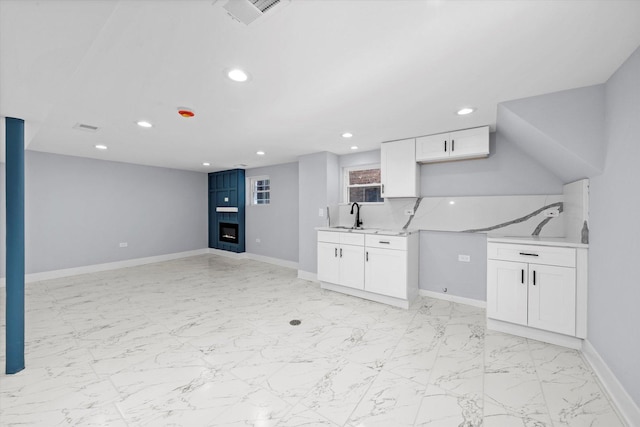 unfurnished living room featuring recessed lighting, a sink, light marble finish flooring, a fireplace, and baseboards
