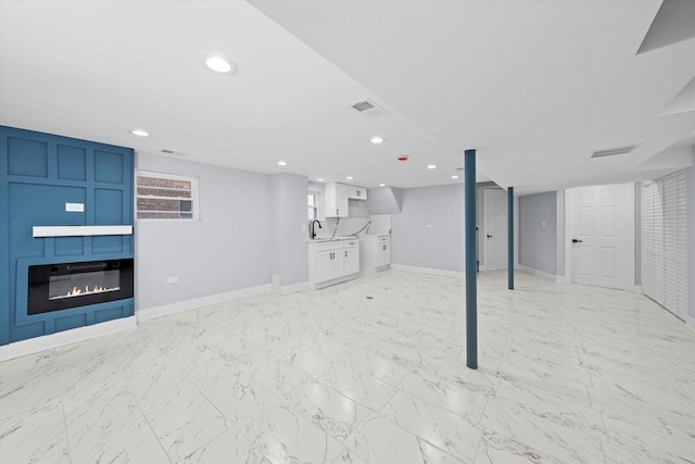 basement featuring a glass covered fireplace, a sink, baseboards, and recessed lighting