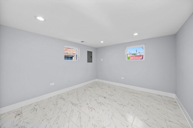 empty room with electric panel, baseboards, healthy amount of natural light, recessed lighting, and marble look tiles