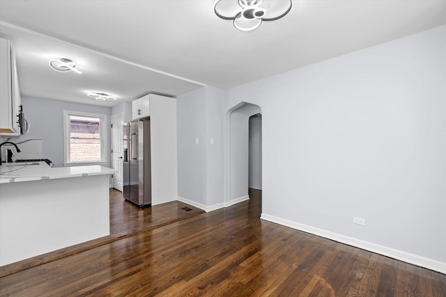 unfurnished living room with arched walkways, dark wood finished floors, baseboards, and a sink