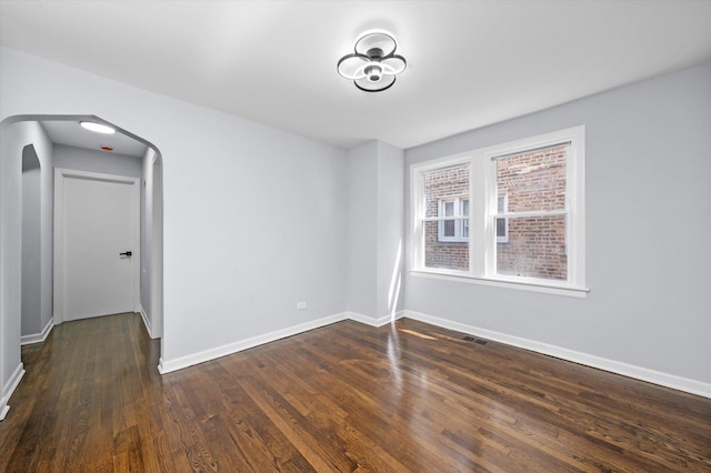 empty room with dark wood-style floors, baseboards, and arched walkways