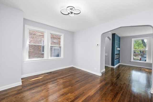 spare room featuring wood finished floors, arched walkways, and baseboards