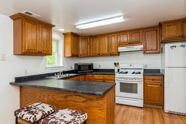 kitchen with white appliances, under cabinet range hood, a sink, brown cabinetry, and recessed lighting