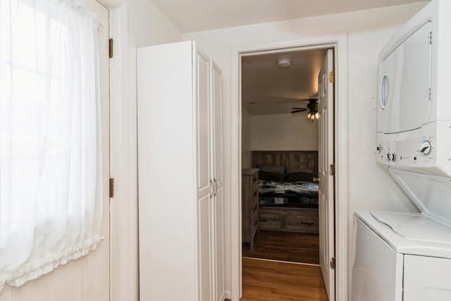 laundry room with stacked washing machine and dryer, a ceiling fan, and wood finished floors