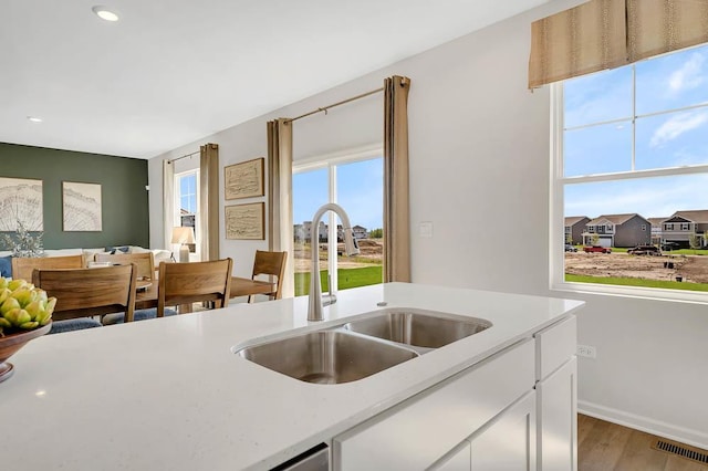 kitchen with a sink, wood finished floors, light countertops, white cabinetry, and recessed lighting