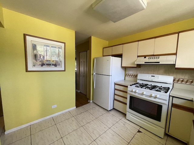 kitchen with white appliances, under cabinet range hood, light countertops, tasteful backsplash, and baseboards